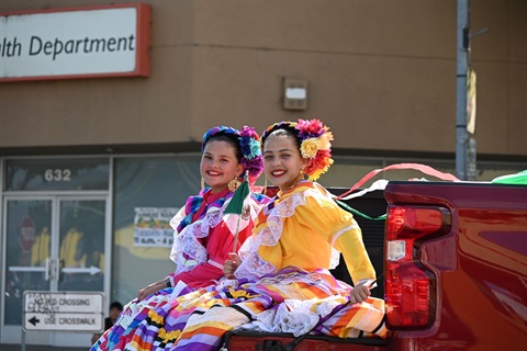 2 Folklorico dancers in the back of a red truck in a parade